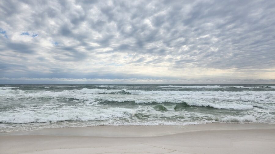 Overcast sky above a gray-blue ocean with white-capped waves rolling onto a pale sandy shore. For the post Strengths, Personal and Professional