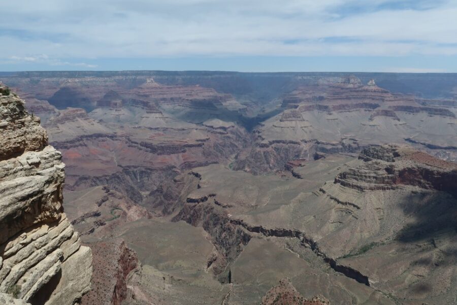 Panoramic view of the Grand Canyon with layered red rocks and deep crevices under a blue sky; canyon cliffs stretch to the horizon.